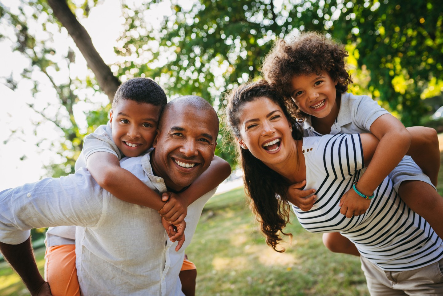 Family of four smiling and playing outdoors by trees