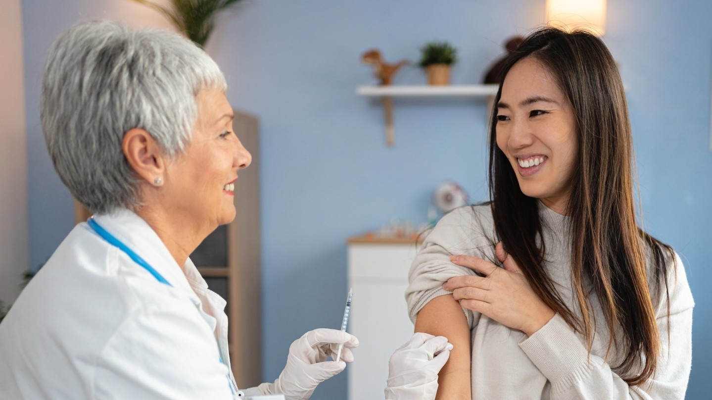 Asian woman smiling and getting a flu vaccination shot